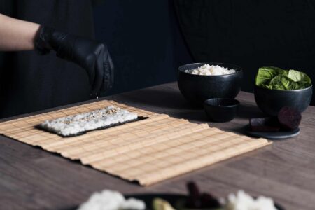 Sushi-Bambusrolle mit Seetangpapier und Reis der mit GewĂĽrzen bestreut wird | Sushi Deluxe